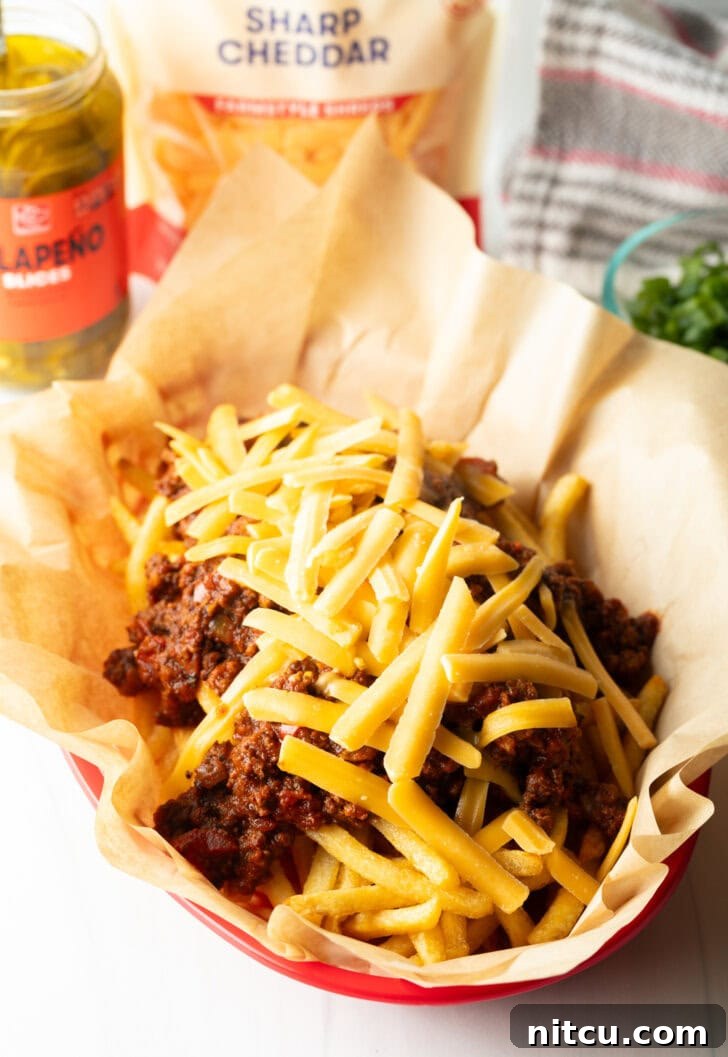 Smothered Chili Cheese Fries 9 A rustic basket lined with parchment paper, filled with crispy french fries generously topped with a rich, hot chili and a lavish sprinkling of shredded cheddar cheese, which has just begun to melt.