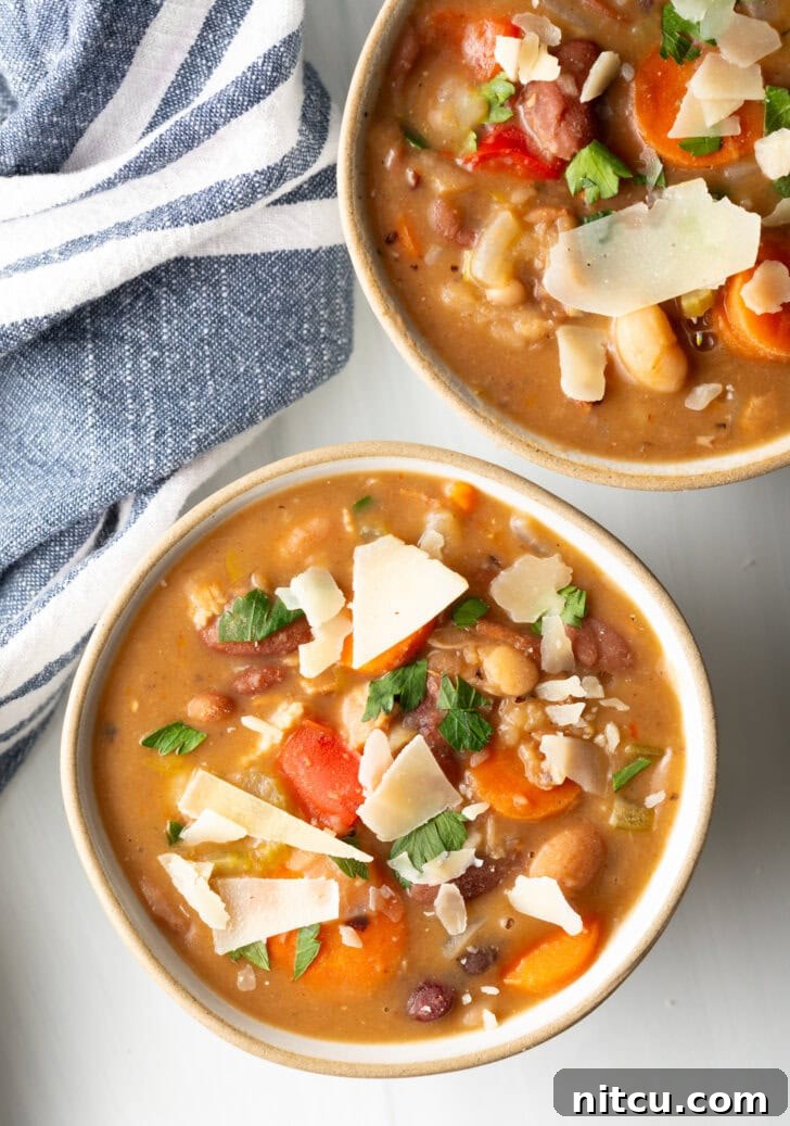 Two white bowls of 15 bean soup, garnished with shaved parmesan.