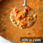 Top down view soup made with 15 beans and veggies in a large cooking pot. A metal ladle is showing a spoonful to camera.