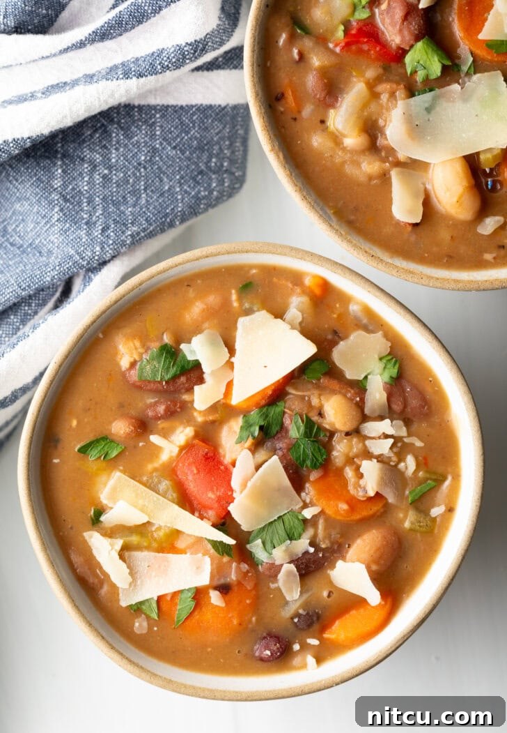 Two white bowls of 15 bean soup, garnished with shaved parmesan.