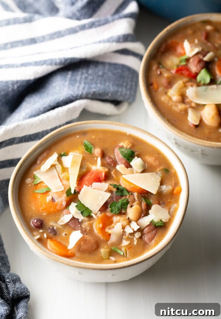 Two white bowls of 15 bean soup, garnished with shaved parmesan.