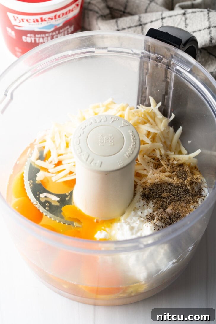 Effortless Egg Bites 5 Various ingredients including shredded cheese, cottage cheese, whole eggs, and spices are placed inside a food processor, ready for blending.