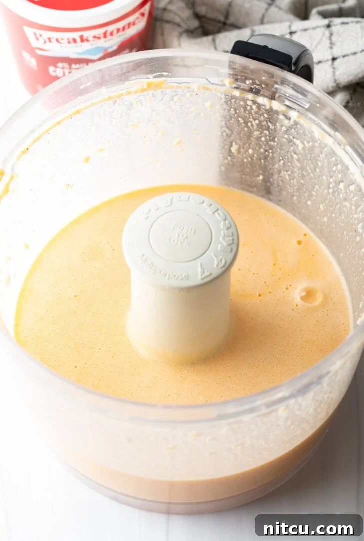 Effortless Egg Bites 6 A food processor contains a smooth, light yellow egg mixture, indicating it has been thoroughly blended.