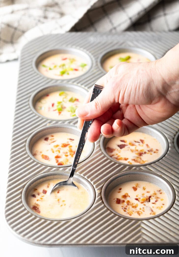 Effortless Egg Bites 8 A hand uses a metal spoon to add the blended egg mixture to individual cups in a metal muffin pan.