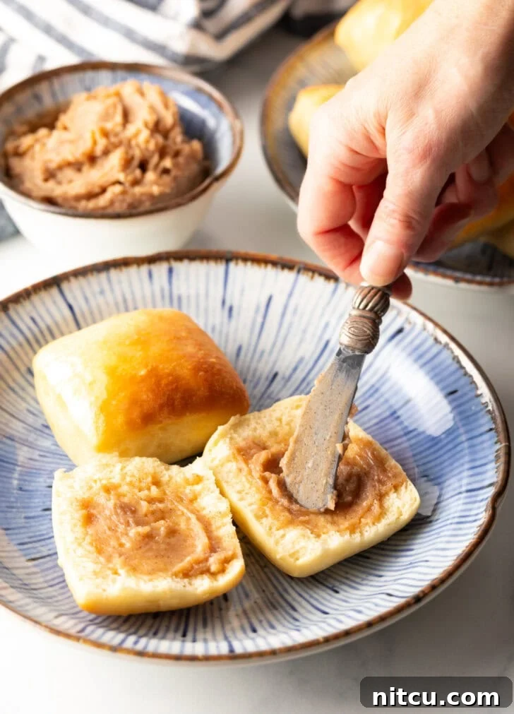 Hand using a small knife to spread cinnamon butter on both sides of an open yeast roll.