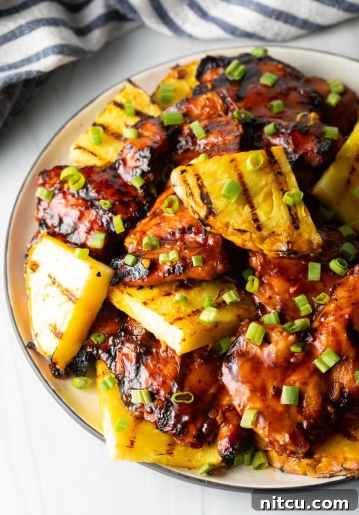 Tropical Glazed BBQ Chicken 2 Huli Huli Chicken Recipe - Top down view of sticky chicken pieces topped with chopped scallions and grilled slices of pineapple, showcasing its delicious caramelization.