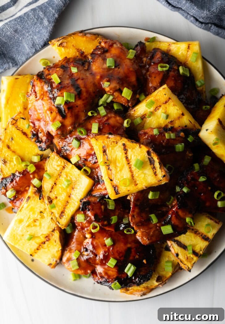 Tropical Glazed BBQ Chicken 4 Top down view of sticky huli huli chicken pieces topped with chopped scallions and grilled slices of pineapple, ready to be served.