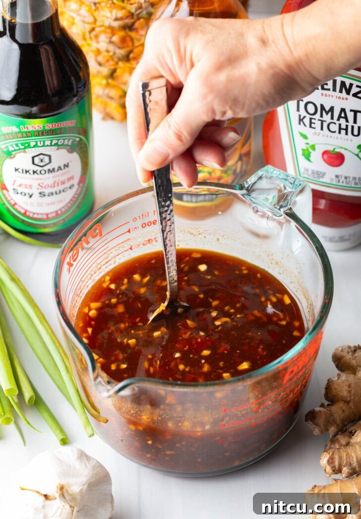 Tropical Glazed BBQ Chicken 7 Hand using metal spoon to stir the Hawaiian chicken marinade in a large glass measuring cup, ensuring all ingredients are well combined.