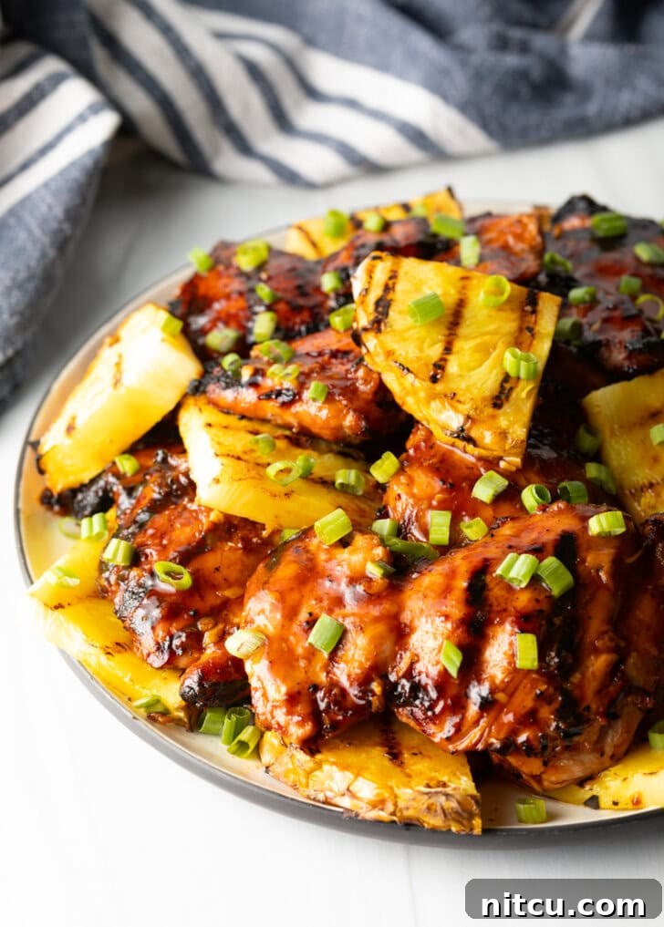 Tropical Glazed BBQ Chicken 9 Sticky huli huli chicken pieces topped with chopped scallions and grilled slices of pineapple, showcasing the perfect glaze.