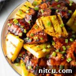 Tropical Glazed BBQ Chicken 10 Top down view of sticky chicken pieces topped with chopped scallions and grilled slices of pineapple.