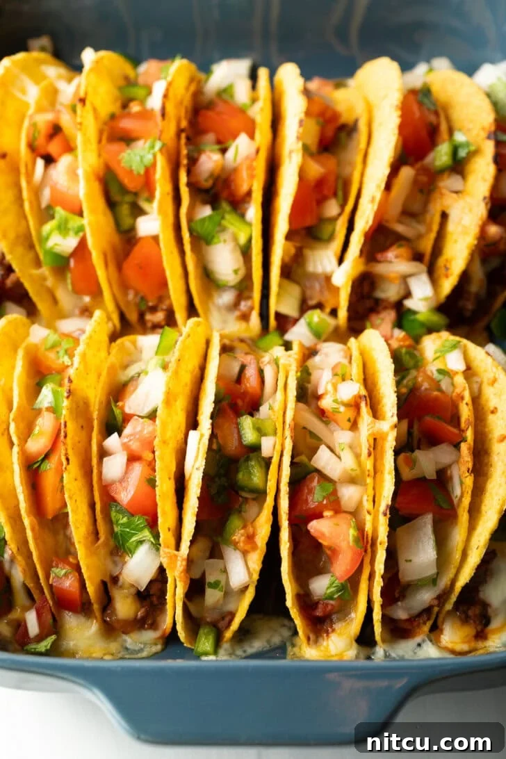 Effortless Baked Tacos 2 Two rows of a dozen loaded yellow corn hard shell tacos, standing upright in a large baking dish, fresh out of the oven.