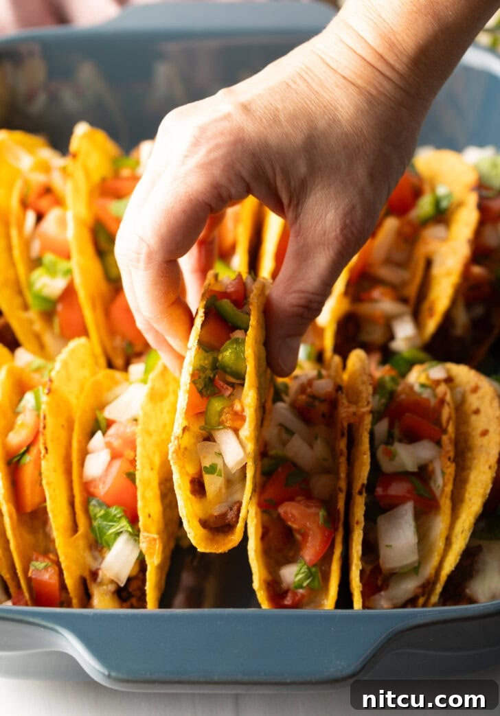Effortless Baked Tacos 11 A hand picking up a single taco from the baked array in the tray, showcasing its crispy shell and generous filling.