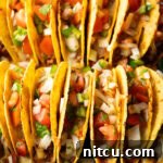 Effortless Baked Tacos 12 Two rows of a dozen loaded yellow corn hard shell tacos, standing upright in a large baking dish, ready to be served.