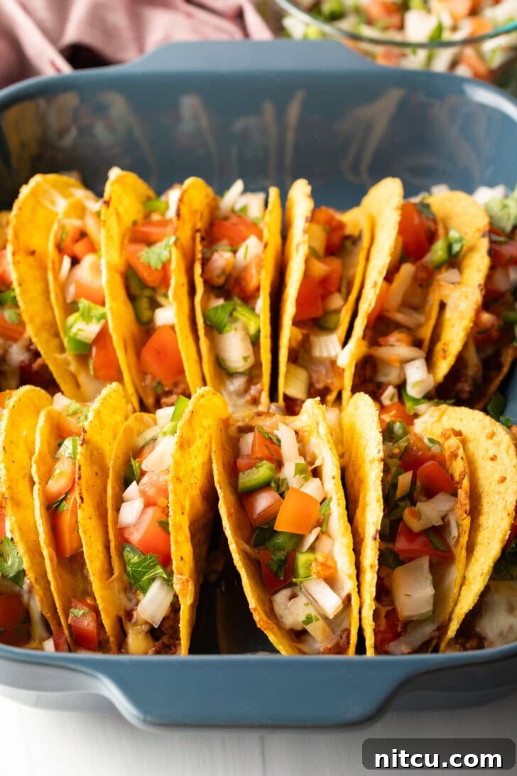Effortless Baked Tacos 4 Two rows of a dozen loaded yellow corn hard shell tacos, standing upright in a large baking dish, ready for the oven.