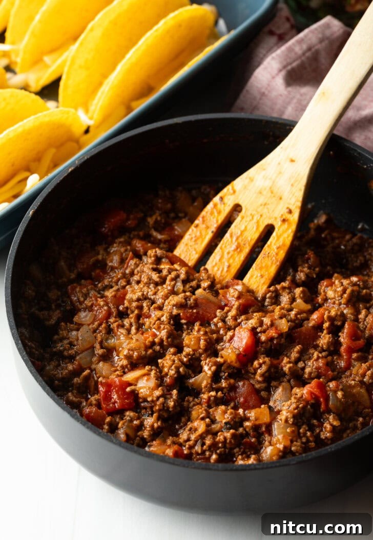 Effortless Baked Tacos 5 Wooden spatula stirring ground beef taco mixture in a large black deep skillet, browning evenly.