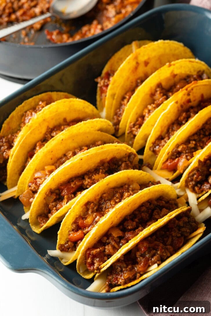 Effortless Baked Tacos 7 Ground beef mixture being added to yellow corn tortilla shells arranged in a baking dish.