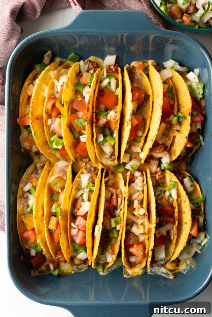 Effortless Baked Tacos 10 Two rows of a dozen loaded yellow corn hard shell tacos, standing upright in a large baking dish, ready to be served.
