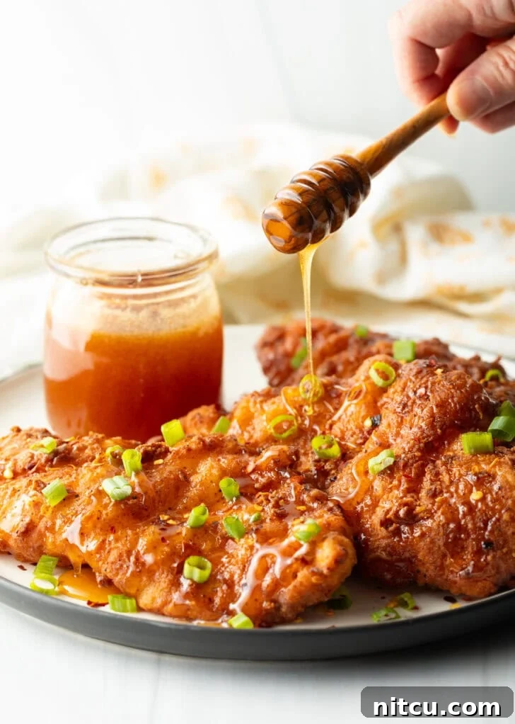 Sweet Heat Chicken 4 A hand expertly drizzling a generous stream of golden hot honey sauce over three pieces of freshly fried chicken, with green onions and a honey jar in the frame.