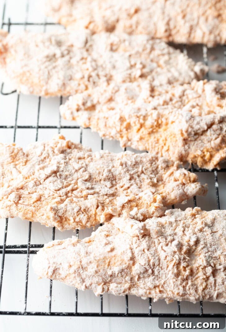 Sweet Heat Chicken 7 Five thinly cut chicken breasts, perfectly dredged and evenly spaced on a wire rack, ready to be fried to a golden crisp.