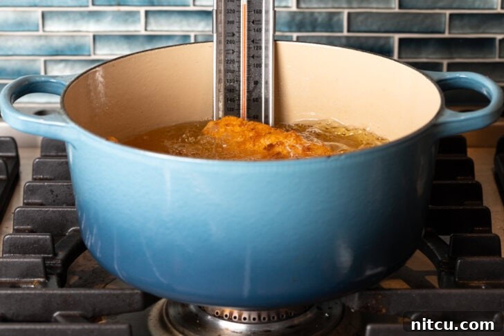 Sweet Heat Chicken 8 A blue cooking pot filled with hot oil, actively frying chicken pieces to a golden crisp. A thermometer is clipped to the side, diligently monitoring the oil temperature.