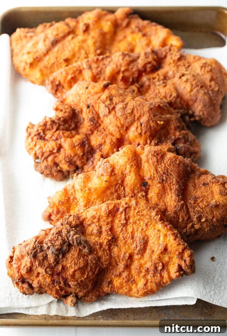 Sweet Heat Chicken 9 Five pieces of perfectly fried chicken breasts, golden brown and resting on paper towels, allowing excess oil to drain after cooking.