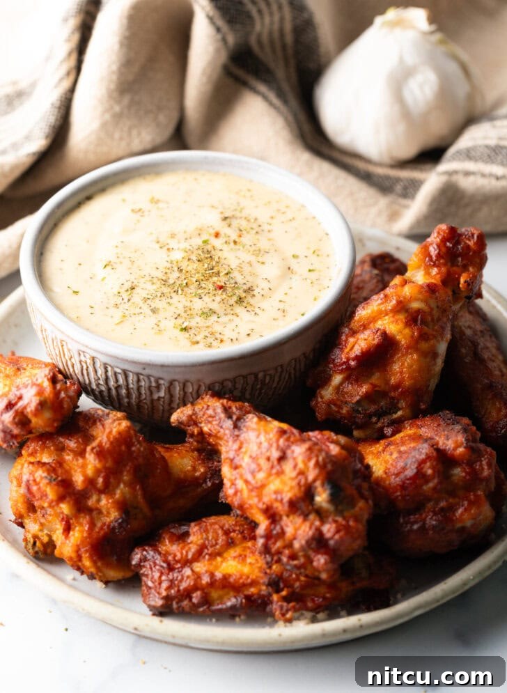 Plate of crispy chicken wings served alongside a small ramekin of homemade garlic parmesan sauce, inviting a delicious dip.