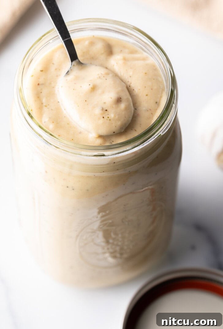 A large glass mason jar filled with luscious homemade garlic and parmesan sauce, with a metal spoon scooping out a generous portion, highlighting its creamy texture.