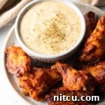 Plate of chicken wings with a ramekin of garlic parmesan sauce, ready for serving.