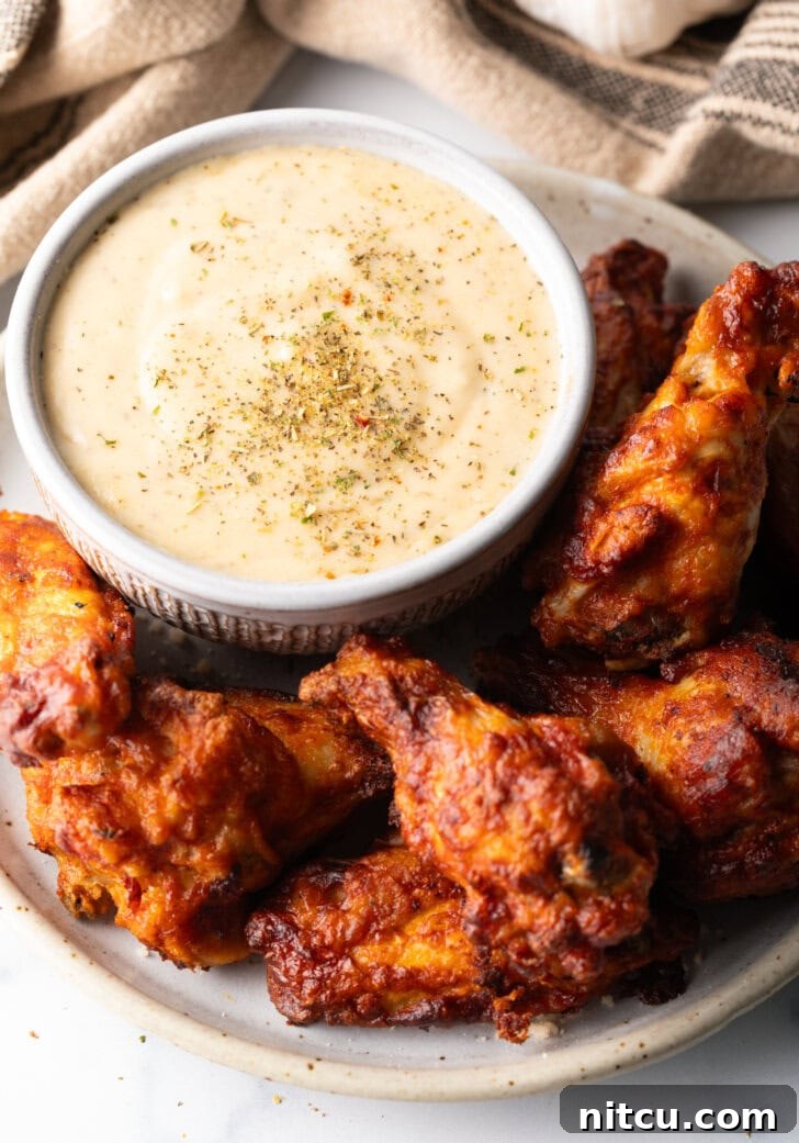 A beautiful plate of golden chicken wings with a side ramekin of creamy garlic parmesan sauce, ready to be enjoyed.