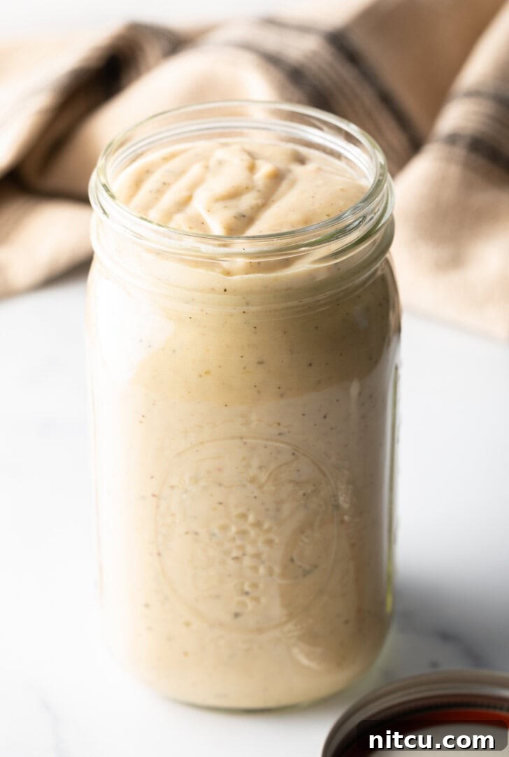 A large glass mason jar filled to the brim with creamy, luscious homemade garlic and parmesan sauce, ready for storage or serving.