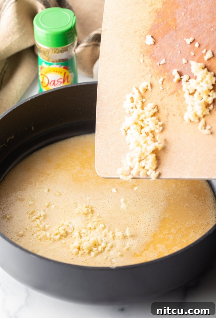 Adding finely minced garlic from a cutting board into a skillet with the prepared sauce roux, ready to infuse flavor.