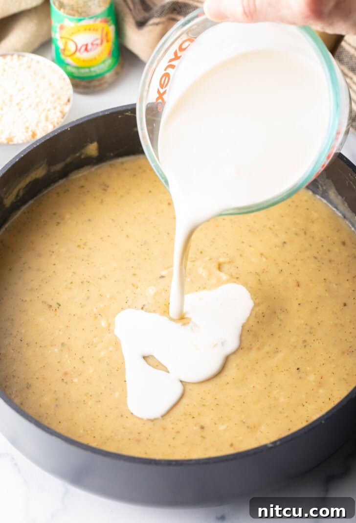 Pouring rich heavy cream from a glass measuring cup into a simmering skillet of fragrant garlic sauce, creating a luxurious base.
