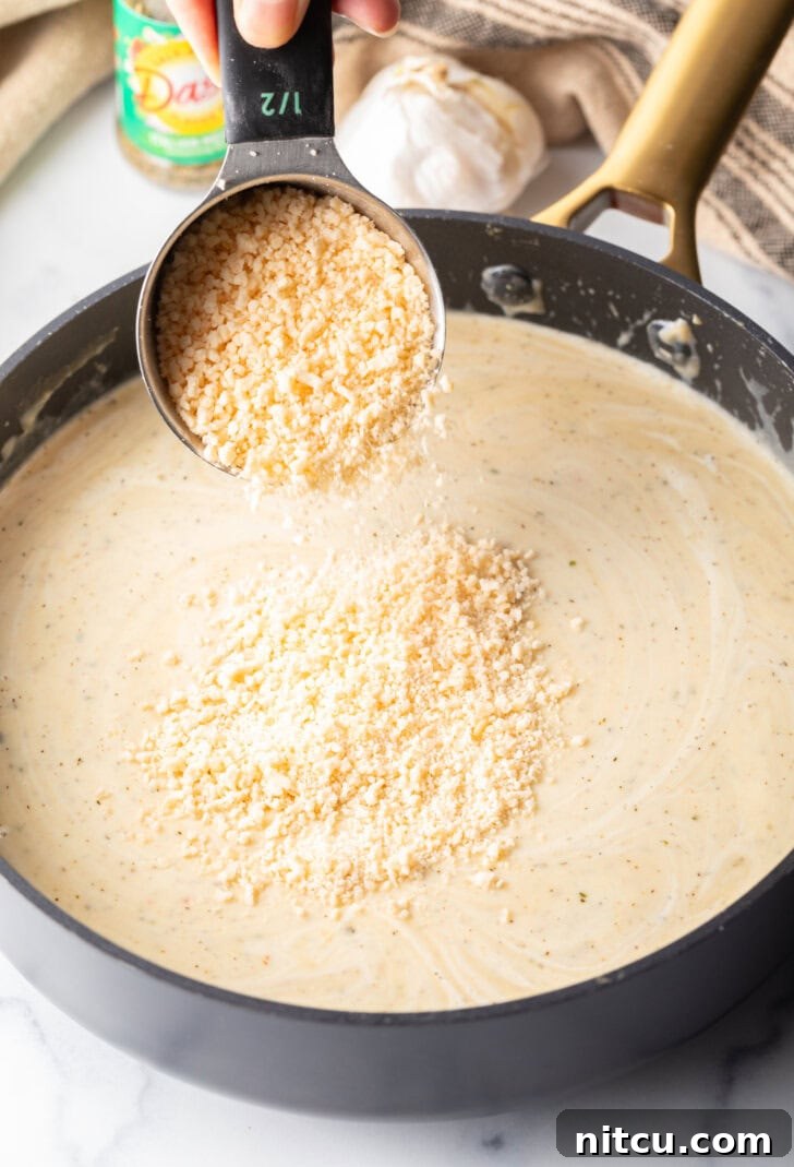 Adding a generous amount of grated parmesan cheese from a measuring cup into the skillet, where it will melt into creamy goodness.