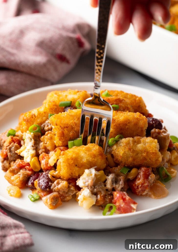 Chuckwagon Tater Tot Casserole 11 White plate with tater tot and ground beef cowboy casserole. A fork is taking a bite from the plate, showing the creamy, meaty filling.