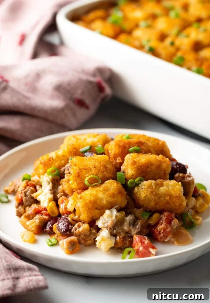 Chuckwagon Tater Tot Casserole 5 A white plate holding a generous serving of cowboy tater tot casserole, showing the layers of ground beef, cheese, and crispy tots.