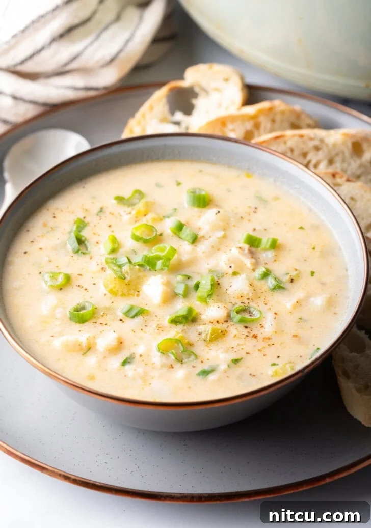 Hearty Seafood Chowder 2 Fish Chowder Recipe in a white bowl, on a gray plate surrounded by slices of bread and a spoon t the side.