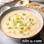 Hearty Seafood Chowder 12 Chowder in a white bowl, on a gray plate surrounded by slices of bread and a spoon t the side.