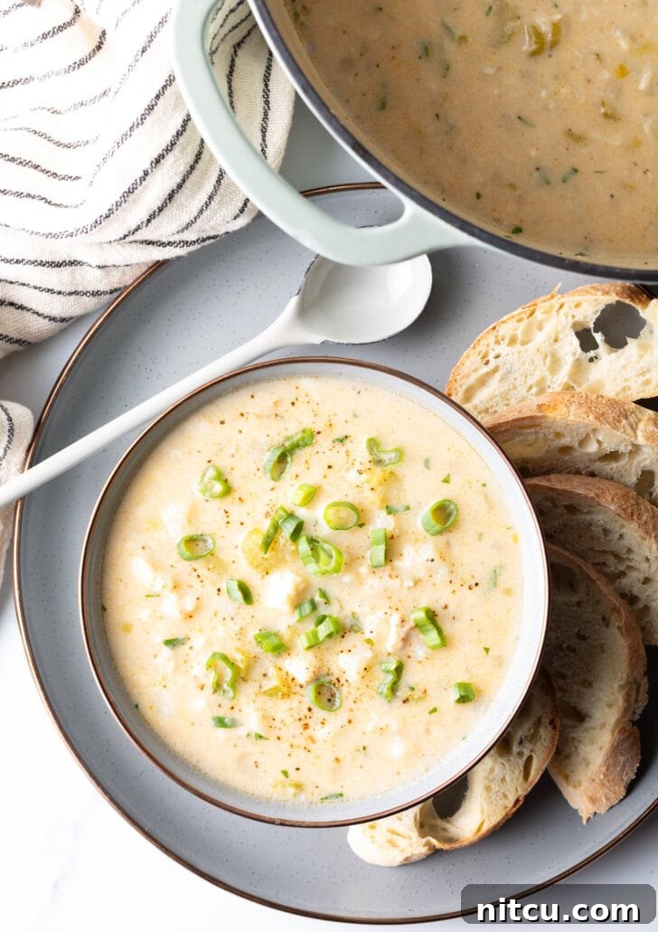 Hearty Seafood Chowder 3 Top down view of the chowder in a white bowl, on a gray plate surrounded by slices of bread and a spoon t the side.