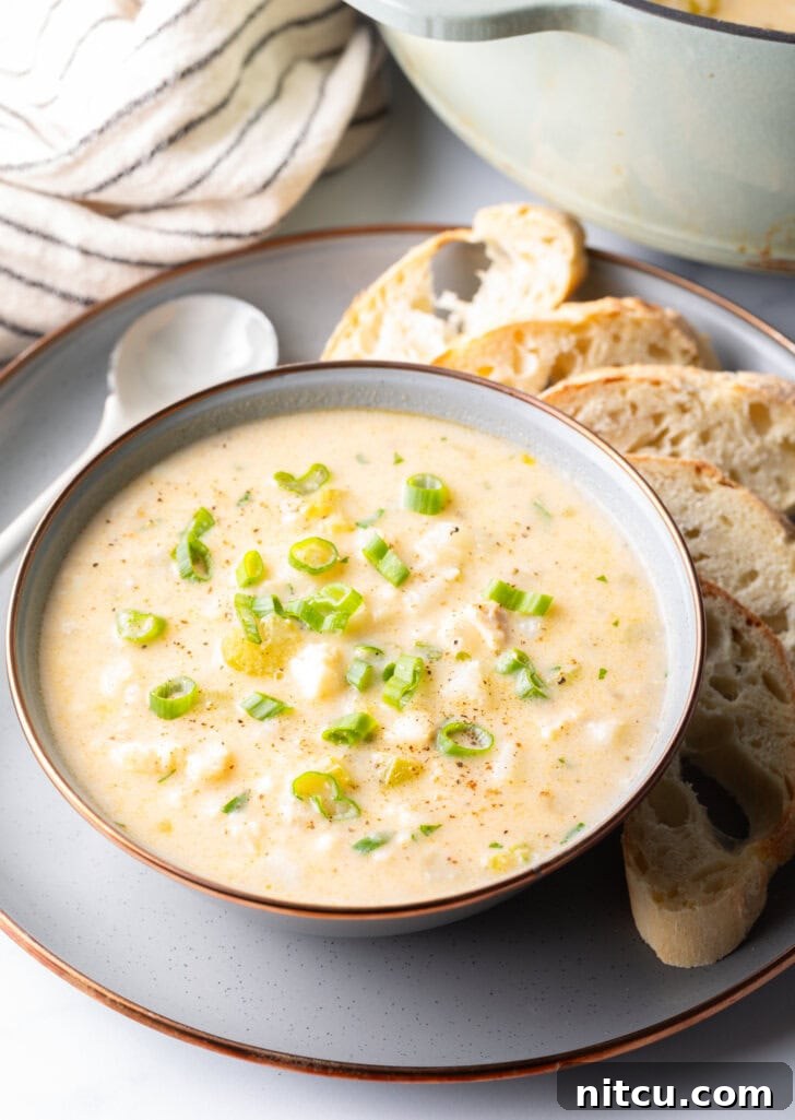Hearty Seafood Chowder 10 Fish Chowder in a white bowl, on a gray plate surrounded by slices of bread and a spoon t the side.