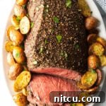 Savory Top Round Roast 12 Cooked beef round roast on a metal baking pan. The front half of the roast has been thinly sliced and the meat is surrounded by roasted baby potatoes.
