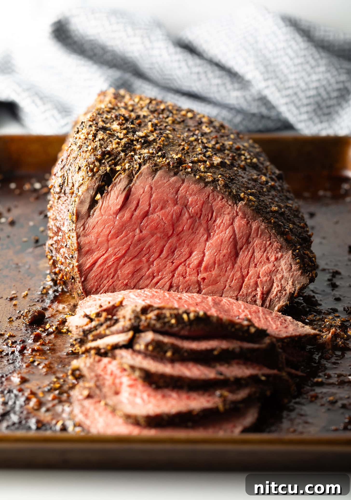 Savory Top Round Roast 3 Cooked beef top round roast on a metal baking pan. The front half of the roast has been thinly sliced.