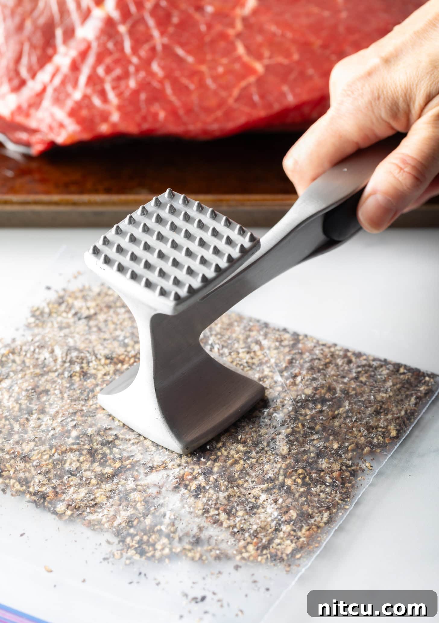 Savory Top Round Roast 6 Hand with metal mallet smashed peppercorns in a plastic zipper bag.