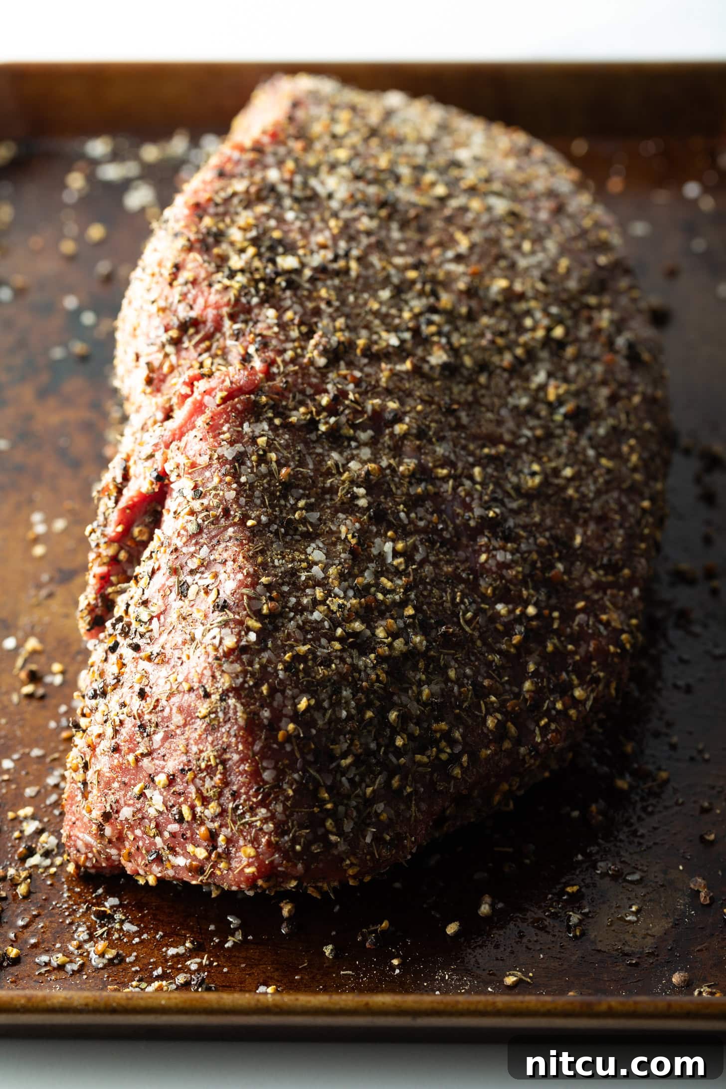 Savory Top Round Roast 8 Raw top round roast coated with pepper rub, on a baking sheet.