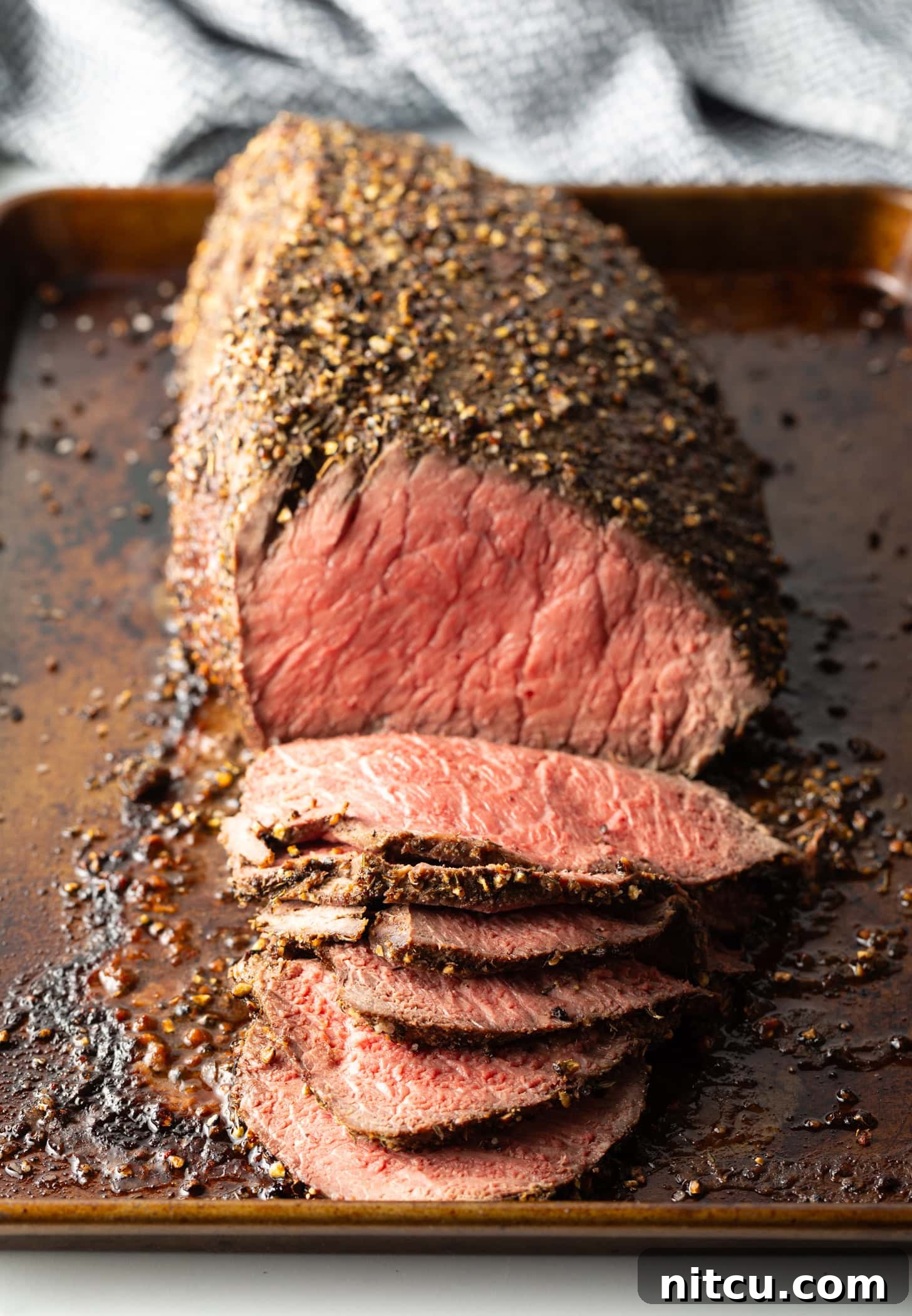 Savory Top Round Roast 10 Cooked beef round roast on a metal baking pan. The front half of the roast has been thinly sliced.