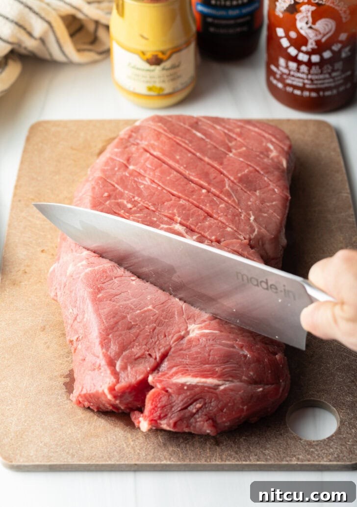 Signature London Broil Marinade 5 Knife scoring a large section of London broil on a cutting board with a criss-cross diagonal pattern.