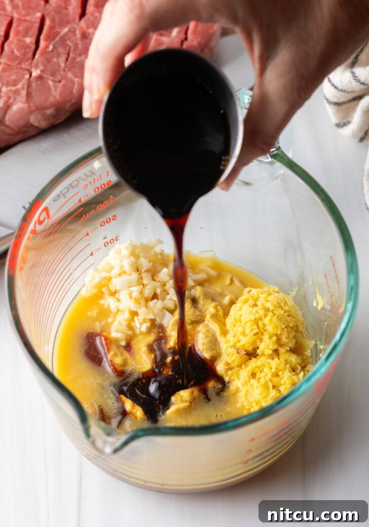 Signature London Broil Marinade 6 Hand adding dark brown sauce to glass measuring cup with marinade ingredients.