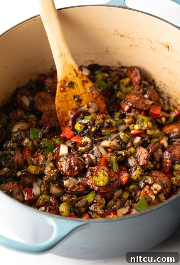 Chopped peppers, onion, and celery in a cooking pot, being stirred by a wooden spatula.