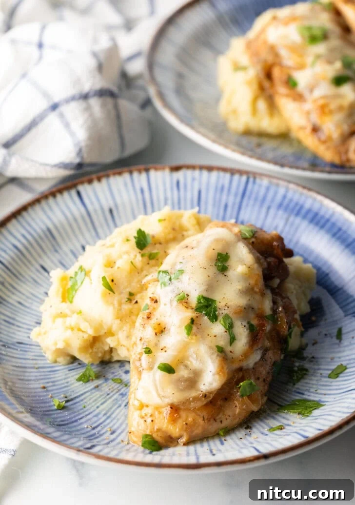 Plate of mashed potatoes topped with French onion chicken breast and gravy.