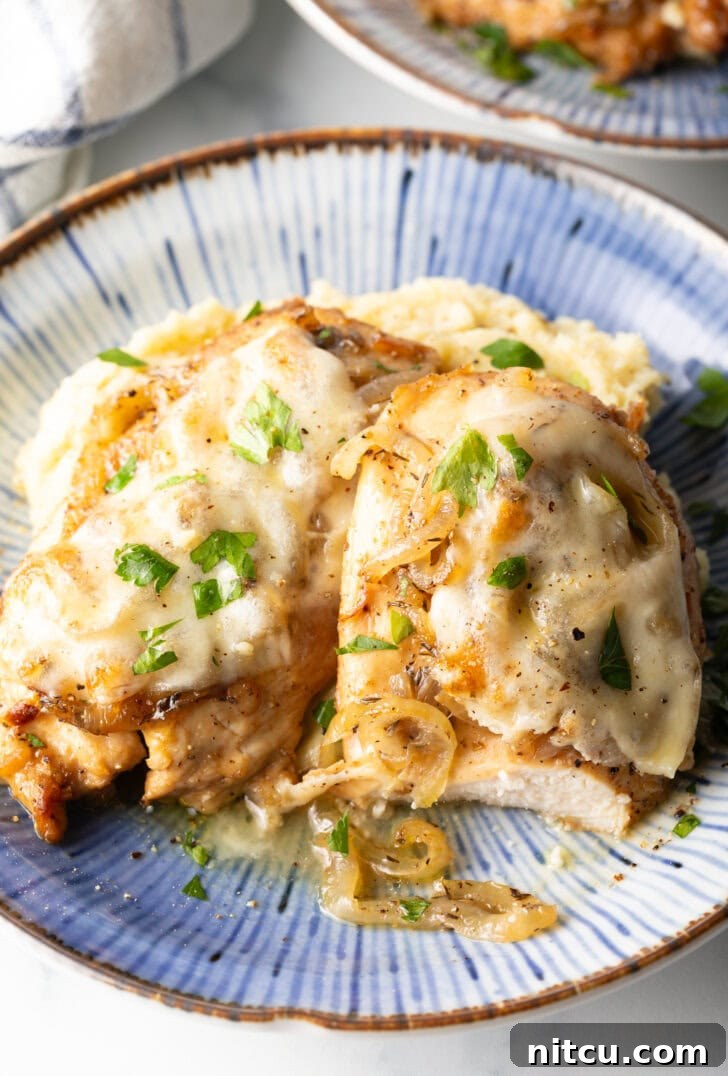 Plate of mashed potatoes topped with 2 French onion chicken breasts and gravy.