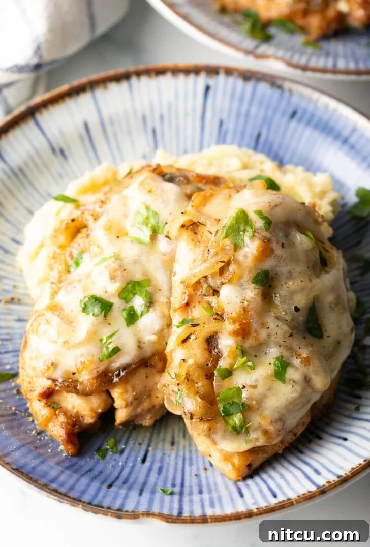 Plate of mashed potatoes topped with 2 French onion chicken breasts and gravy.